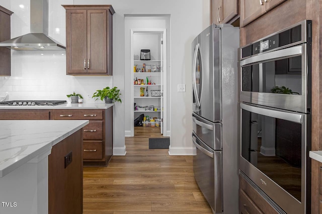 kitchen featuring tasteful backsplash, light stone counters, stainless steel appliances, wall chimney exhaust hood, and dark wood-style flooring