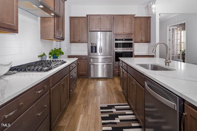 kitchen featuring a sink, under cabinet range hood, backsplash, stainless steel appliances, and dark wood-style flooring