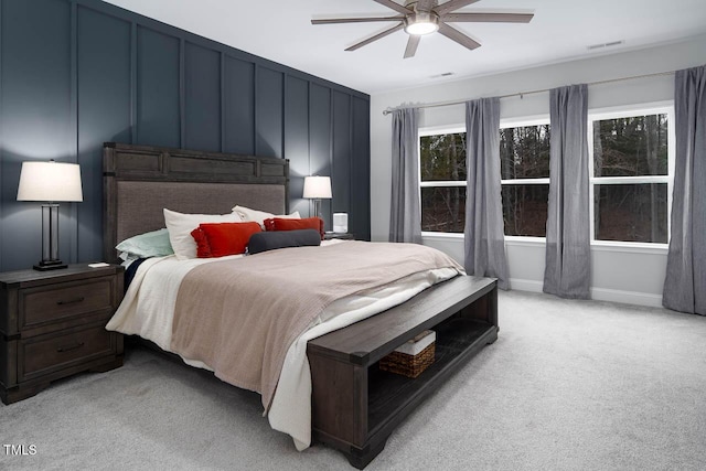 bedroom with ceiling fan, a decorative wall, visible vents, and light carpet