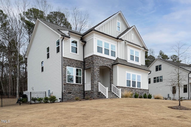 craftsman house with stone siding, board and batten siding, a front yard, and fence