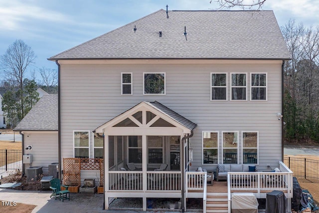 back of property featuring a wooden deck, a shingled roof, fence, and a sunroom