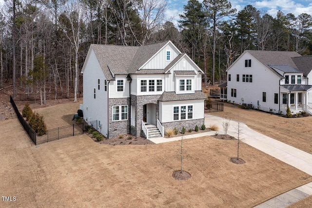 view of front facade featuring board and batten siding, a shingled roof, fence, stone siding, and driveway