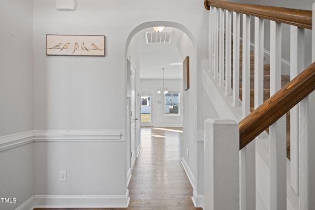 hall featuring baseboards, wood finished floors, visible vents, and arched walkways