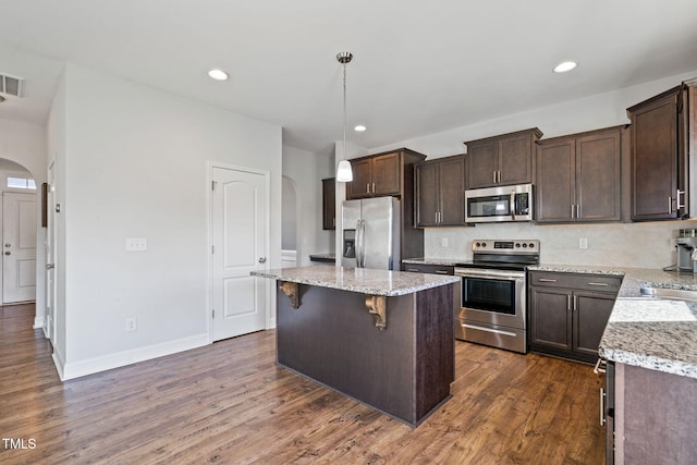 kitchen with dark brown cabinetry, stainless steel appliances, a center island, and arched walkways