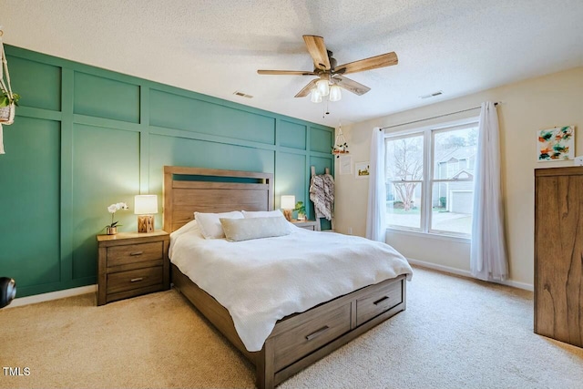 bedroom with visible vents, light colored carpet, a decorative wall, and a textured ceiling