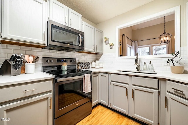 kitchen with decorative light fixtures, stainless steel appliances, a sink, and light countertops