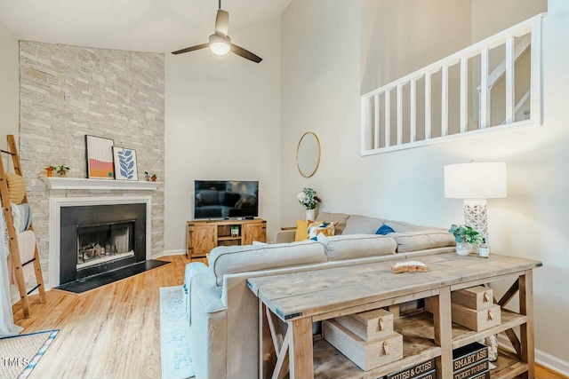 living room featuring a large fireplace, baseboards, a ceiling fan, a towering ceiling, and wood finished floors