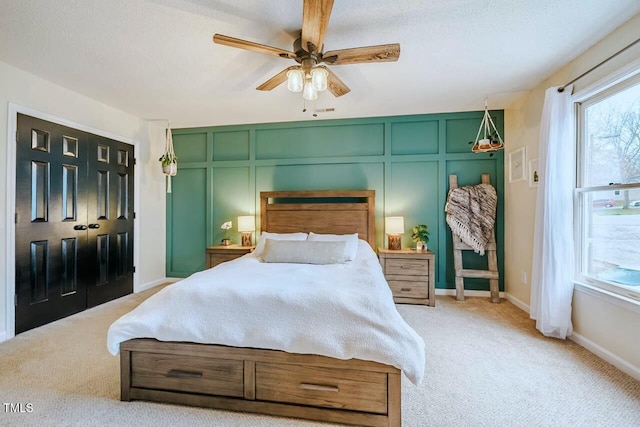 bedroom featuring light carpet, a decorative wall, a textured ceiling, and baseboards