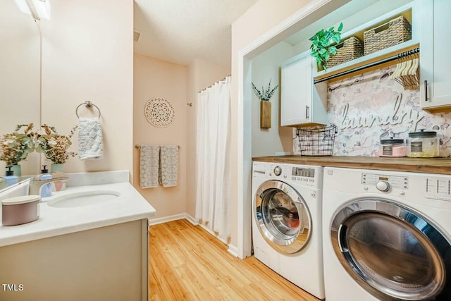 washroom featuring cabinet space, independent washer and dryer, a textured ceiling, light wood-type flooring, and a sink