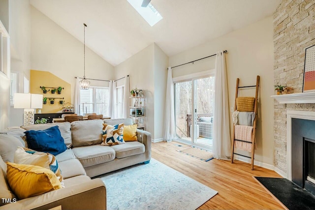 living room with a skylight, light wood-style floors, a fireplace, high vaulted ceiling, and a notable chandelier