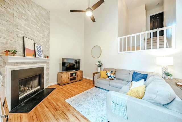 living room with ceiling fan, a fireplace, wood finished floors, a towering ceiling, and baseboards