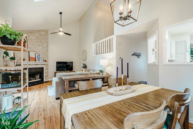 dining space with high vaulted ceiling, a fireplace, light wood finished floors, and ceiling fan