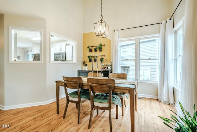 dining area featuring light wood-type flooring, a notable chandelier, a towering ceiling, and baseboards