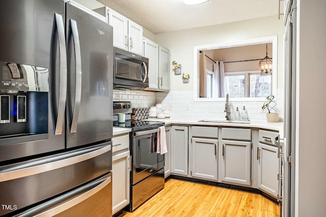 kitchen with pendant lighting, stainless steel appliances, light countertops, backsplash, and a sink