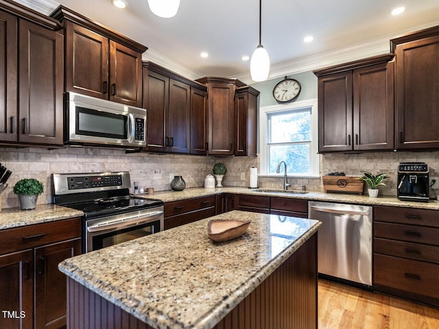 kitchen featuring light stone counters, stainless steel appliances, a sink, hanging light fixtures, and dark brown cabinets