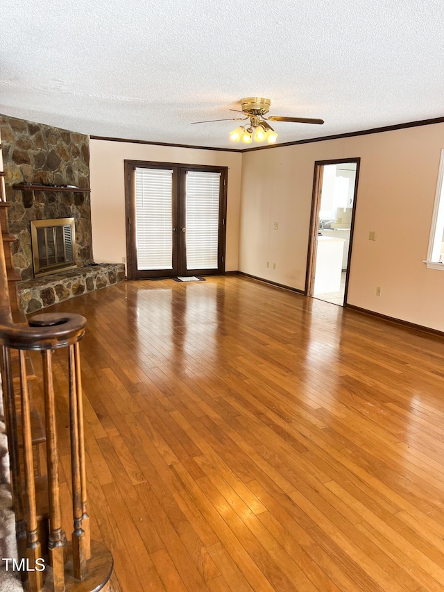 unfurnished living room with french doors, crown molding, a stone fireplace, a textured ceiling, and light wood-type flooring