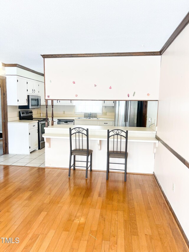 kitchen featuring light wood finished floors, stainless steel appliances, a breakfast bar, and white cabinetry