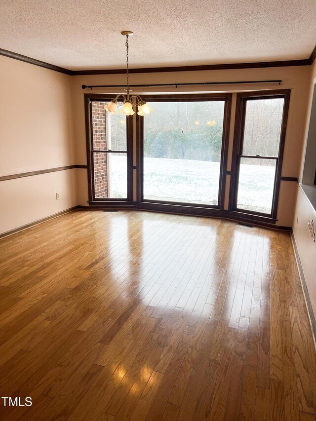 unfurnished room with ornamental molding, a chandelier, a textured ceiling, and wood finished floors