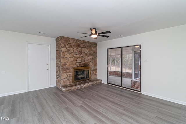 unfurnished living room with visible vents, a ceiling fan, a stone fireplace, wood finished floors, and baseboards