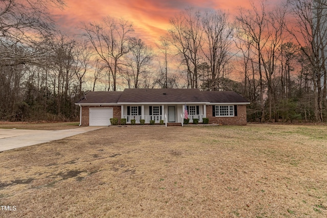 ranch-style house featuring brick siding, covered porch, an attached garage, driveway, and a front lawn