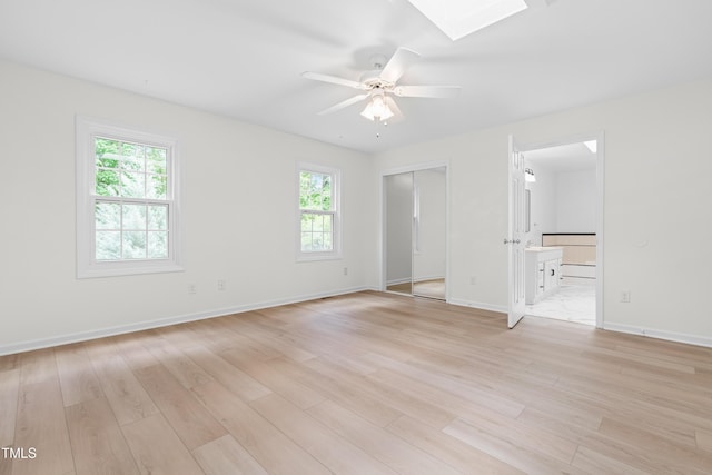 unfurnished bedroom featuring multiple windows, a skylight, and light wood-style flooring