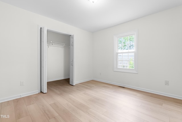 unfurnished bedroom featuring light wood finished floors, baseboards, and a closet