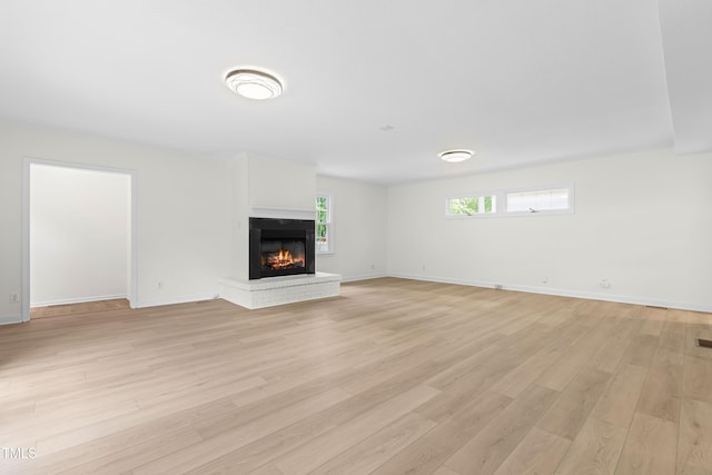 unfurnished living room with light wood finished floors, a brick fireplace, and baseboards