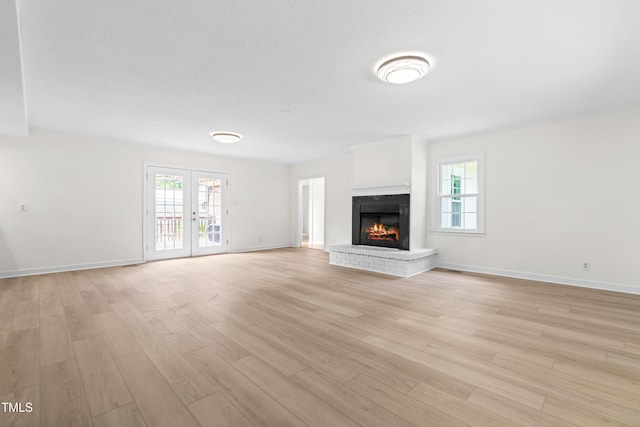 unfurnished living room featuring plenty of natural light, light wood-style flooring, and a brick fireplace