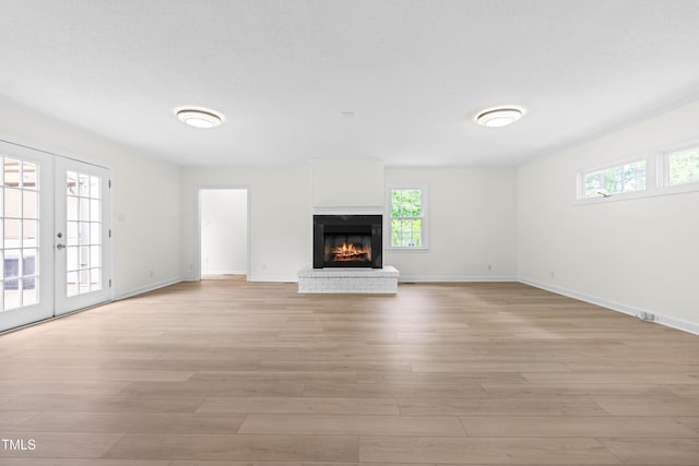 unfurnished living room featuring light wood finished floors, baseboards, a fireplace, and french doors