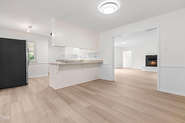 kitchen with freestanding refrigerator, a peninsula, light countertops, light wood finished floors, and a wainscoted wall