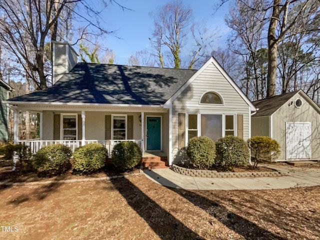 view of front of home featuring covered porch, an outbuilding, a chimney, and a storage shed