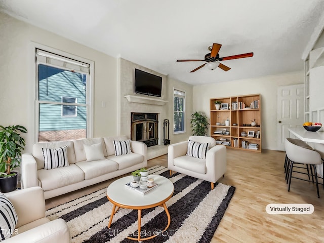 living area featuring a large fireplace, a ceiling fan, and light wood finished floors