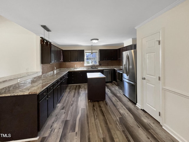 kitchen featuring dark wood finished floors, a kitchen island, stainless steel appliances, pendant lighting, and a sink