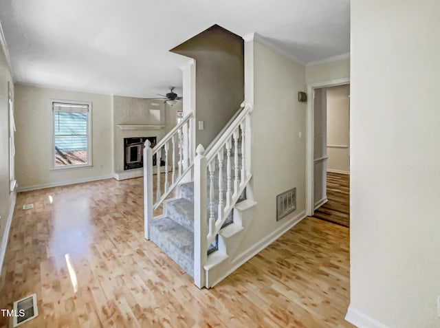 stairs featuring a ceiling fan, visible vents, a fireplace, and wood finished floors