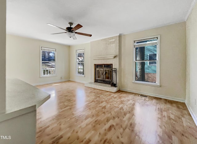 unfurnished living room featuring a large fireplace, baseboards, visible vents, a ceiling fan, and wood finished floors