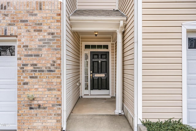 view of exterior entry with brick siding and roof with shingles