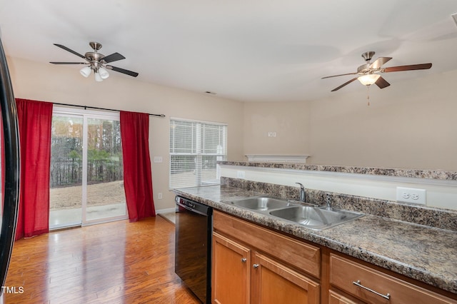 kitchen with a sink, brown cabinets, dishwasher, light wood finished floors, and dark countertops