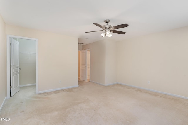 interior space featuring light carpet, ceiling fan, a spacious closet, and baseboards