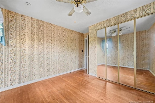 unfurnished bedroom with a ceiling fan, wood finished floors, baseboards, wallpapered walls, and a closet