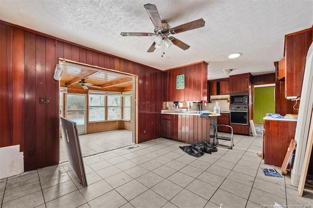 kitchen featuring light countertops, oven, light tile patterned floors, black microwave, and a peninsula