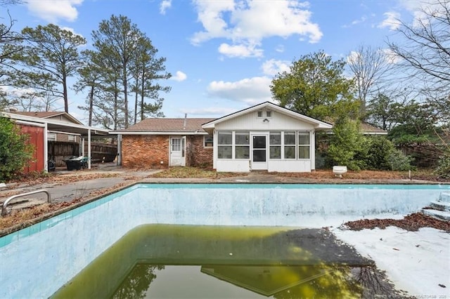 exterior space with brick siding, a sunroom, and an empty pool