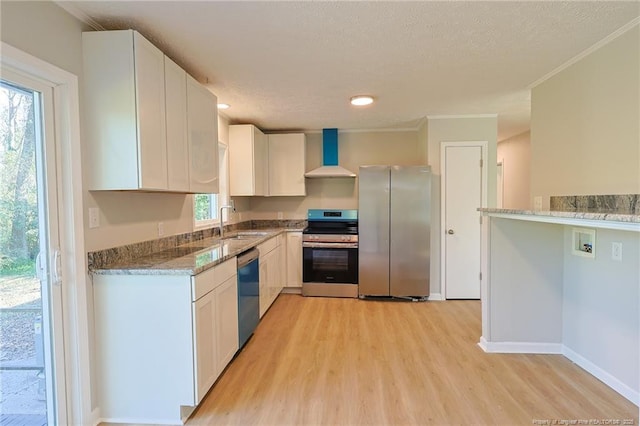 kitchen with a sink, wall chimney exhaust hood, light stone counters, appliances with stainless steel finishes, and white cabinetry