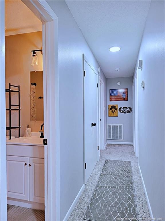 hall with a sink, visible vents, light carpet, and baseboards