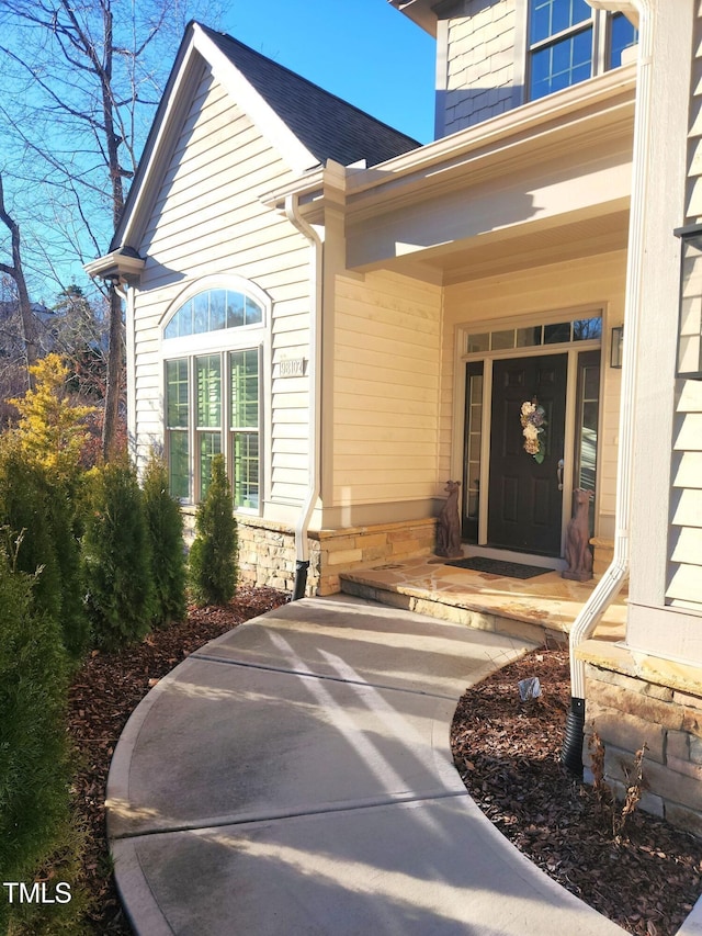 doorway to property featuring a porch and roof with shingles