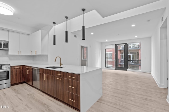 kitchen featuring stainless steel appliances, light countertops, hanging light fixtures, white cabinets, and a sink