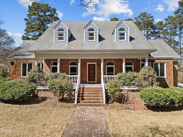 cape cod house with covered porch, brick siding, and roof with shingles