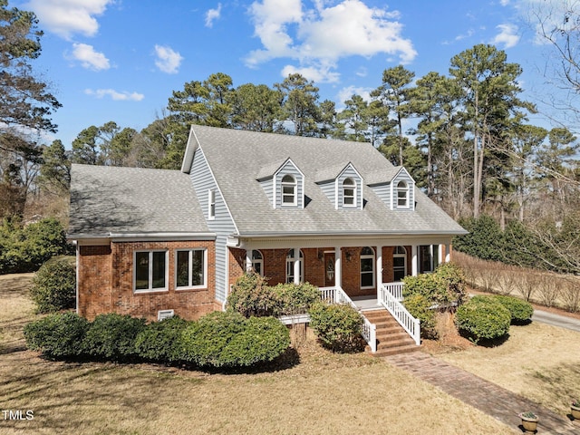 cape cod-style house featuring a porch, a front yard, brick siding, and roof with shingles