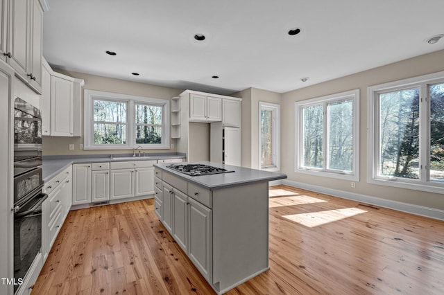 kitchen with oven, stainless steel gas cooktop, a sink, white cabinets, and light wood finished floors