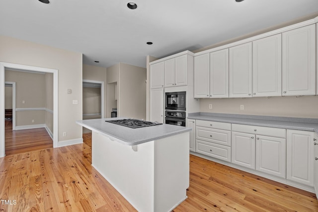 kitchen with light wood-style flooring, a kitchen island, light countertops, black appliances, and white cabinetry