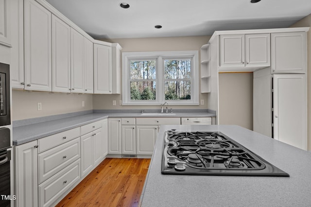 kitchen featuring light wood finished floors, light countertops, white cabinetry, a sink, and black gas stovetop